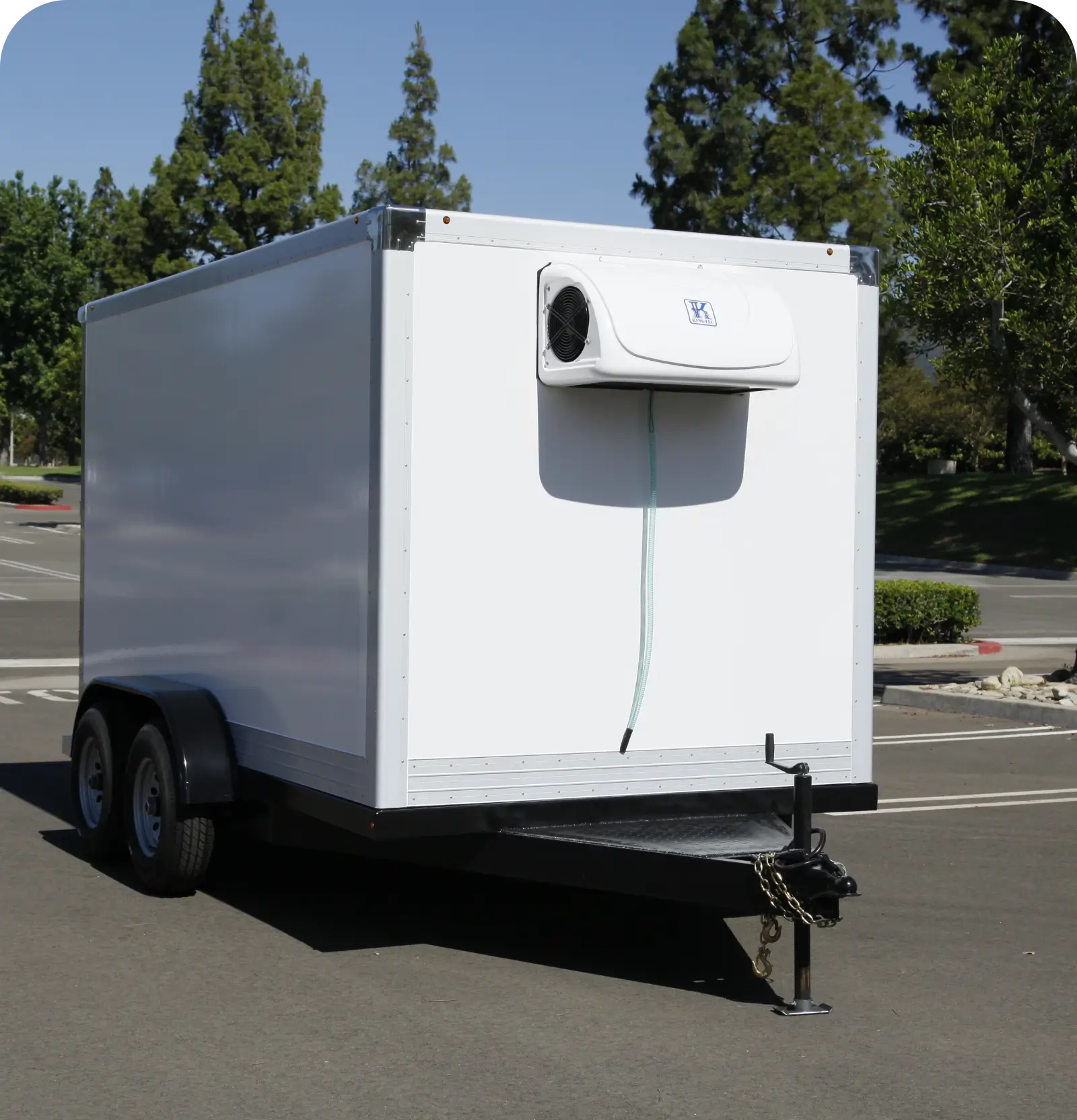 A white enclosed trailer parked outdoors near trees.