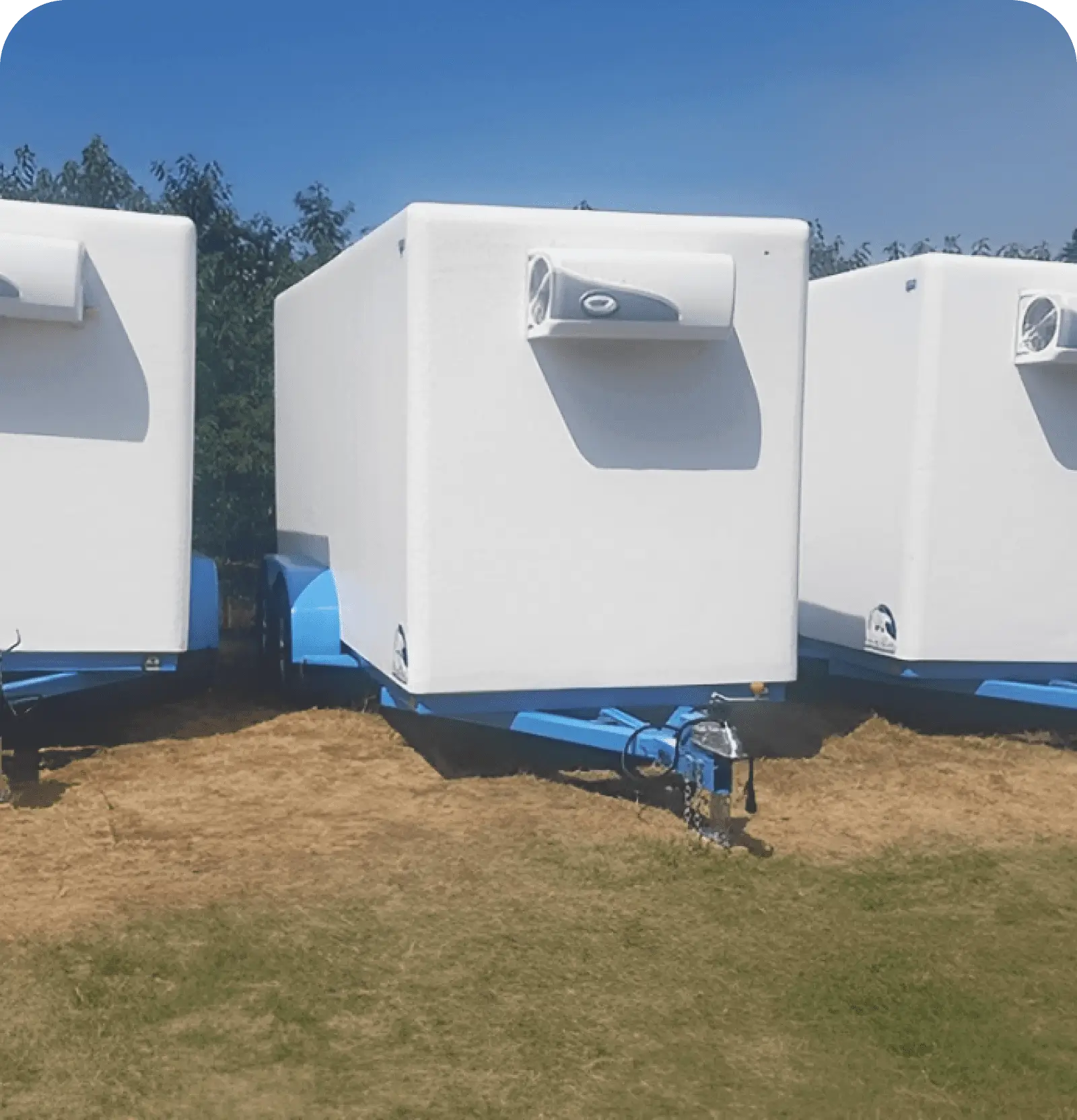 Three white mobile units parked on grass under a clear blue sky.